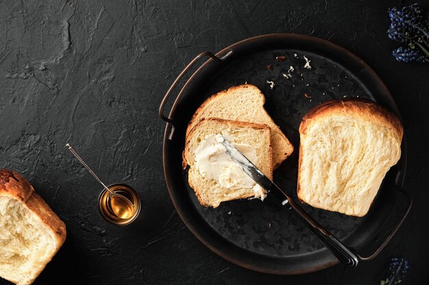 Pão de brioche doce na bandeja com manteiga de faca e mel em uma superfície vintage escura plano leigo tradicional conceito de assado de brioche francês doce