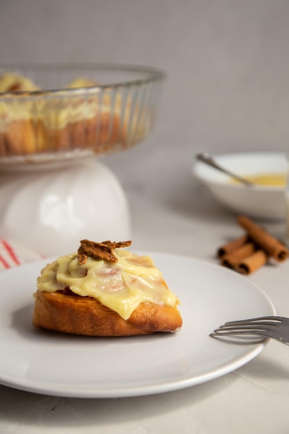 pão de canela com glacê e paus de canela com um copo de leite em um fundo cinza claro