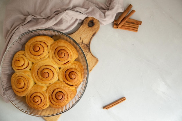 pão de canela com glacê e paus de canela com um copo de leite em uma vista de fundo cinza claro