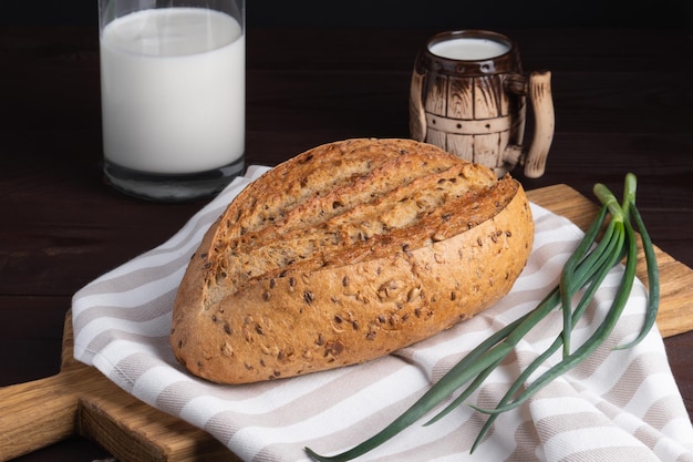 Pão de centeio caseiro fresco bando caneca de argila de cebola e garrafa de leite na tábua de madeira
