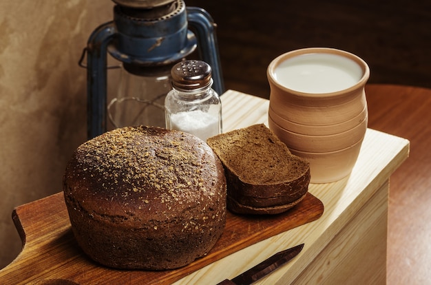 Pão de centeio com sal em uma tábua, pote de cerâmica com leite. natureza morta em estilo rústico