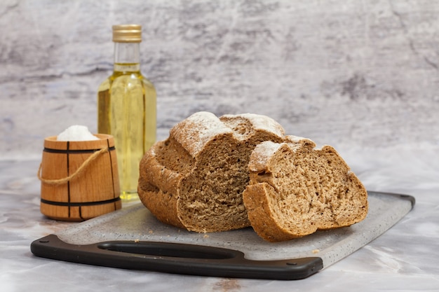 pão de centeio em uma tábua de cortar, uma garrafa de óleo de girassol e uma adega de sal de madeira