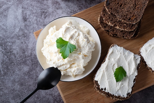 Pão de centeio em uma tábua de madeira com requeijão e ricota e ervas Decorado com ervas verdes