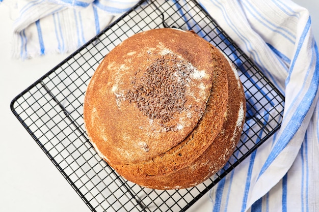 Pão de centeio redondo caseiro em uma cremalheira de metal com um pano