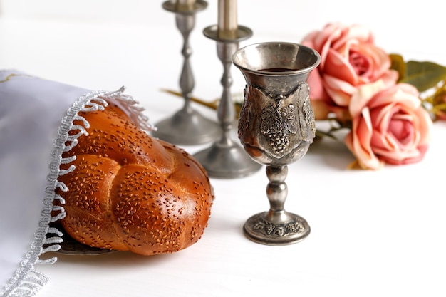 Pão de chalá coberto com um guardanapo especial vinho de shabbat e velas em fundo branco ritual de shabat judaico tradicional shabbat shalom