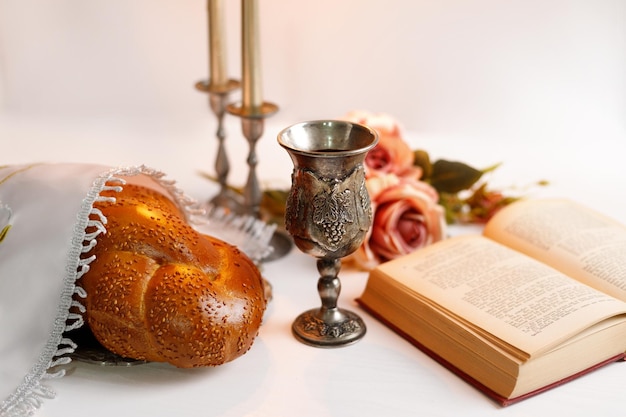 Pão de chalá coberto com um guardanapo especial vinho shabbat torá e velas em fundo branco Ritual judaico tradicional de Shabbat Shabbat Shalom