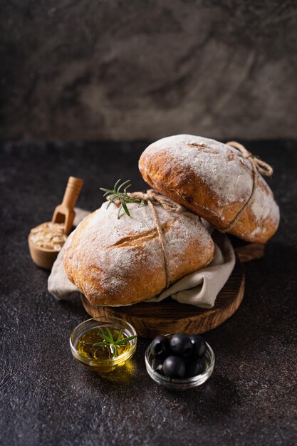 Pão de ciabatta artesanal orgânico fresco com ervas, azeite e azeitonas em fundo escuro