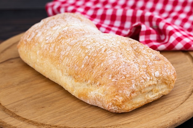 Foto pão de ciabatta em uma placa de corte na mesa de madeira escura.