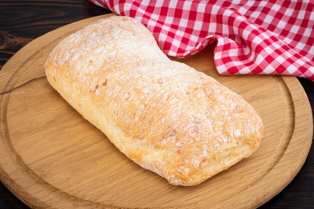 Pão de ciabatta em uma placa de corte na mesa de madeira escura.