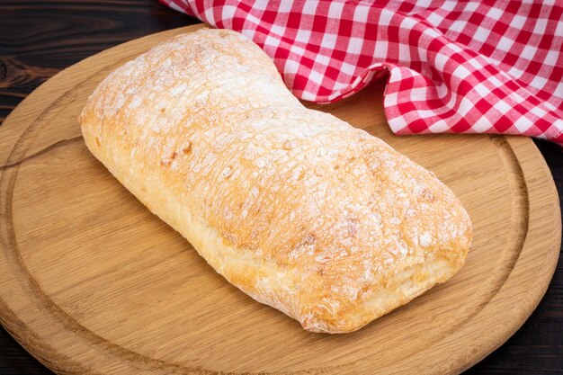 Pão de ciabatta em uma placa de corte na mesa de madeira escura.