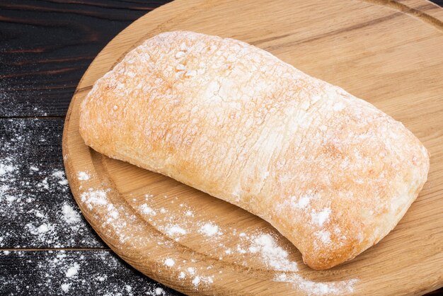Pão de ciabatta em uma placa de corte na mesa de madeira escura.