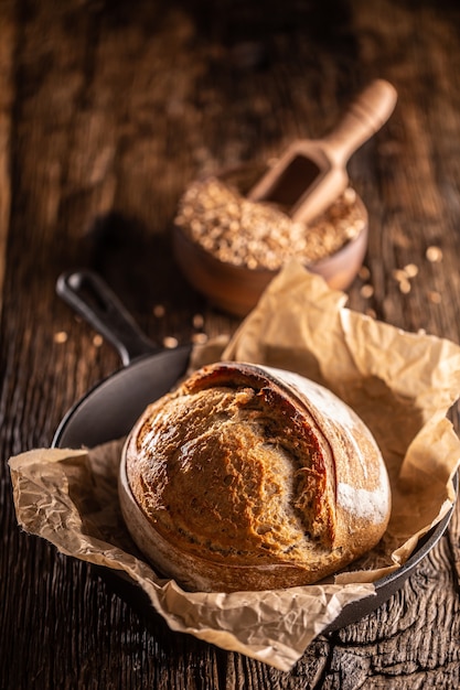 Pão de fermento rústico crocante recém-assado sobre o papel manteiga na assadeira de liga com uma tigela de madeira cheia de grãos de trigo.