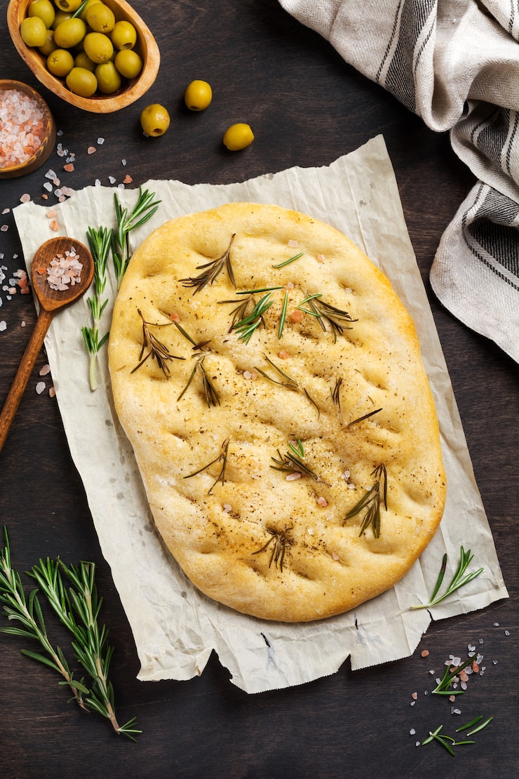 Foto pão de focaccia tradicional italiana assando com temperos aromáticos e alecrim no fundo da mesa rústica de madeira velha. vista do topo