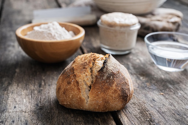 Pão de pão caseiro recém-assado ao lado de ingredientes farinha água e fermento em tábuas de madeira rústicas