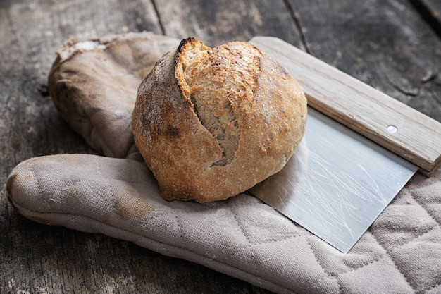 Pão de pão de fermento recém-assado com deliciosa crosta dourada colocada em um cortador de massa e luva de cozinha