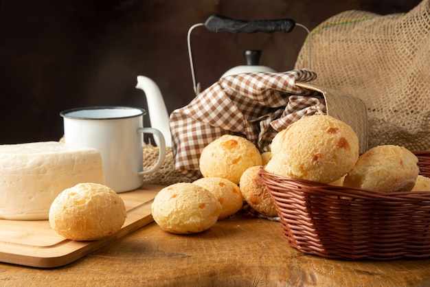 Pão de queijo, arranjo de café da manhã brasileiro, pão de queijo, queijo branco, chaleira e acessórios, fundo abstrato escuro, foco seletivo.