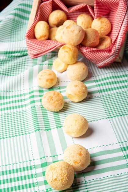 Pão de queijo brasil, pãezinhos de queijo caindo de uma caixa sobre uma toalha de mesa xadrez verde, foco seletivo.