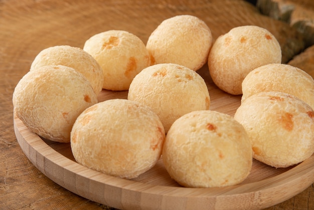 Pão de queijo brasileiro disposto em prato de madeira sobre prato de madeira rústica