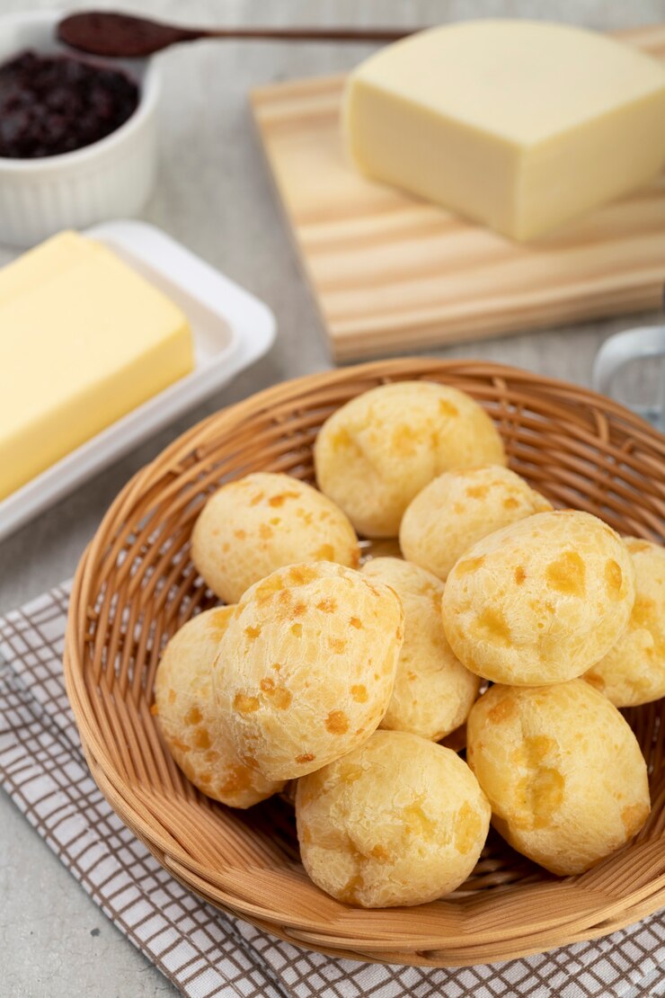 Foto pão de queijo típico brasileiro em uma cesta com manteiga, geléia e queijo