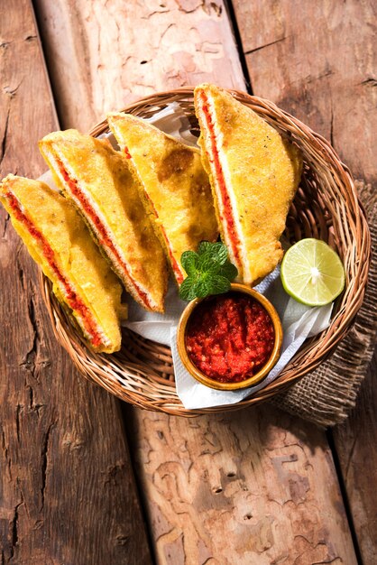 Pão de sanduíche Pakora ou pakoda (forma de triângulo) servido com ketchup de tomate, chutney, pimenta verde e fatias de cebola, popular lanche indiano para a hora do chá. Foco seletivo