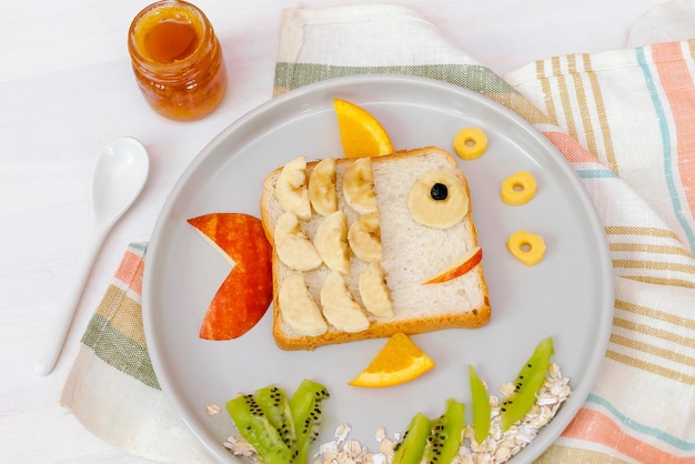 Pão de torrada de sanduíche de forma de peixe fofo engraçado com banana maçã e mel Laranja Doce infantil sobremesa doce café da manhã saudável arte de comida de almoço no prato fundo de madeira close uptop view