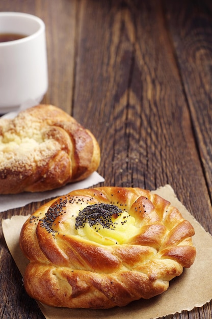 Pão doce com sementes de papoula e xícara de chá na mesa de madeira escura