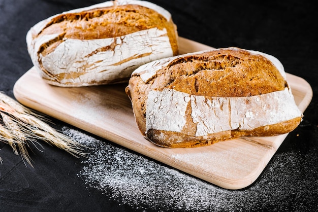 Pão doce e saboroso e trigo em fundo preto de madeira