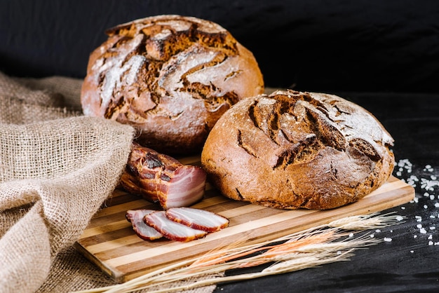 Pão doce e saboroso e trigo em fundo preto de madeira