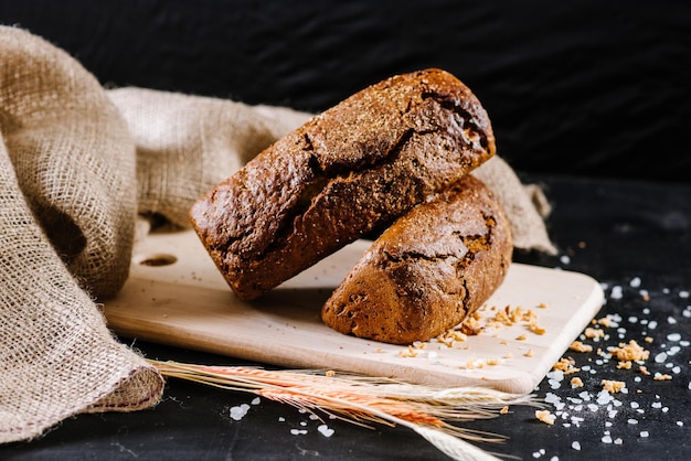 Pão doce e saboroso e trigo em fundo preto de madeira