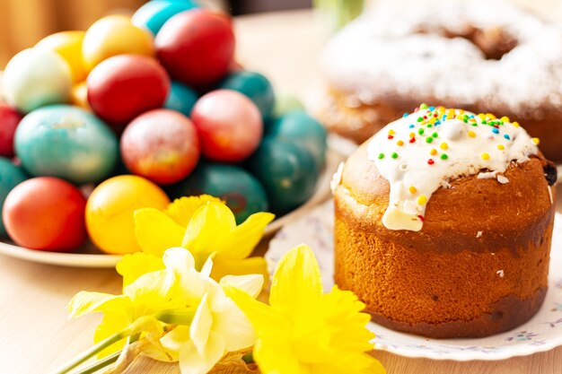 Pão doce ortodoxo da Páscoa, kulich, ovos coloridos e um buquê de narcisos. Luz do sol brilhante. Café da manhã tradicional da Páscoa. Foco seletivo.