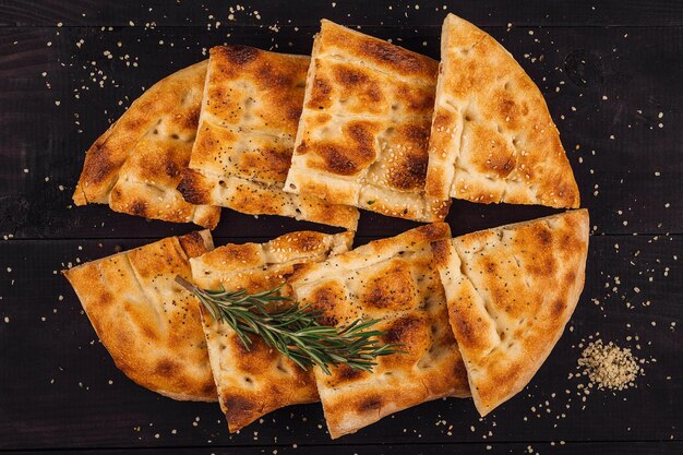 Pão em fatias de pide salpicado de sementes de gergelim e romário em uma mesa de madeira escura