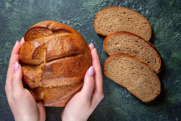 Pão escuro fresco de vista superior com mãos femininas na mesa escura