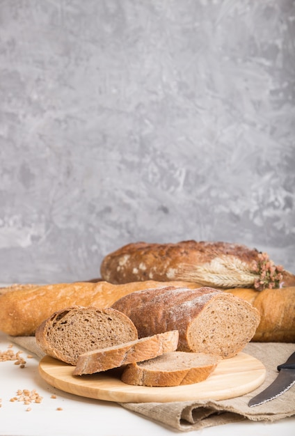 Pão fatiado com diferentes tipos de pão fresco em uma superfície de concreto cinza. Vista lateral, foco seletivo.