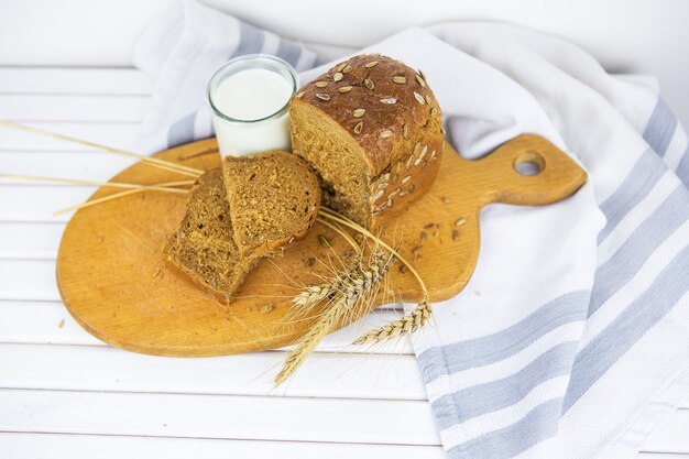 Pão fatiado em uma tábua de madeira, um copo de leite, trigo seco