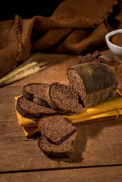 Pão fatiado feito com cacau e chocolate em pano amarelo na mesa de madeira rústica com ingredientes.