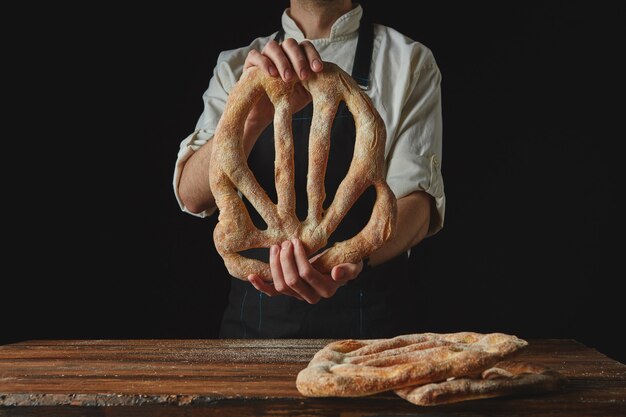 Pão fougas delicioso recém-assado nas mãos de um homem em um fundo preto