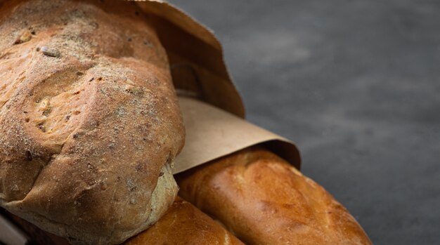 Pão fresco apetitoso e baguete com uma crosta crocante sobre um fundo escuro em um saco de papel. espaço livre à direita, baguete e pão à esquerda.