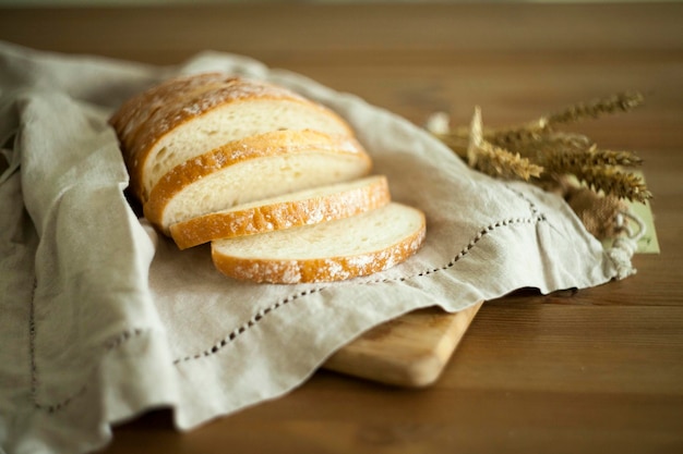 Pão fresco branco sobre os têxteis de linho e mesa de madeira com copo de leite e grãos. Fotografia de alimentos - conceito de padaria. fatia pão de trigo branco caseiro e pano de prato. pão no guardanapo de linho