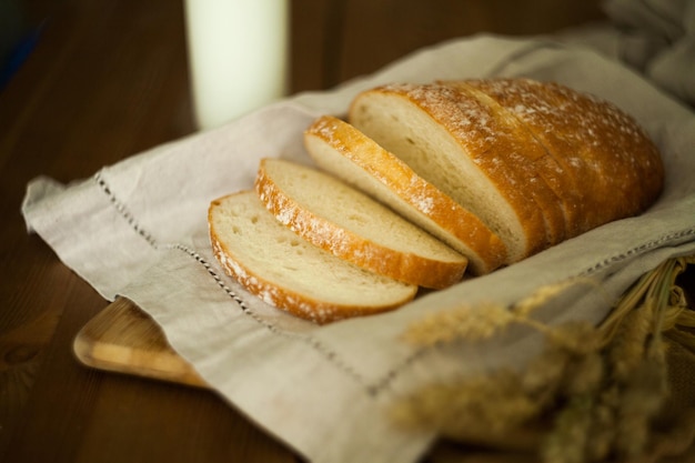 Pão fresco branco sobre os têxteis de linho e mesa de madeira com copo de leite e grãos. Fotografia de alimentos - conceito de padaria. fatia pão de trigo branco caseiro e pano de prato. pão no guardanapo de linho