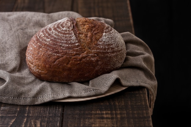 Pão fresco com toalha de cozinha na placa de madeira escura