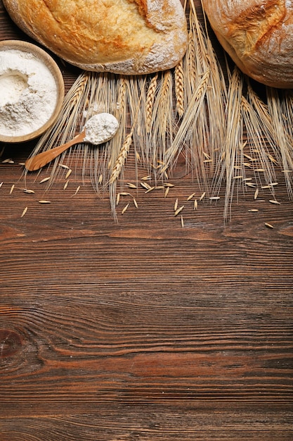 Pão fresco cozido uma tigela de farinha e espigas de trigo no fundo de madeira