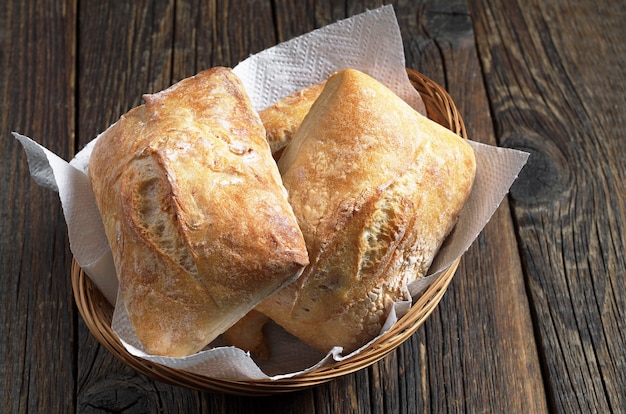 Pão fresco de ciabatta em uma tigela de vime na mesa de madeira escura