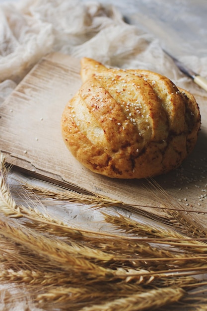 Pão fresco e espigas de trigo no foco seletivo da placa de madeira rústica