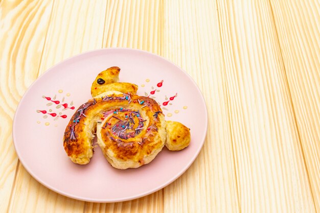 Pão fresco sob a forma de um coelhinho da Páscoa. O conceito de comida de férias infantil. Na placa cerâmica rosa na superfície de madeira.