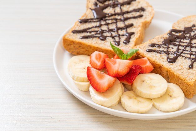 Pão integral torrado com banana fresca, morango e chocolate no café da manhã