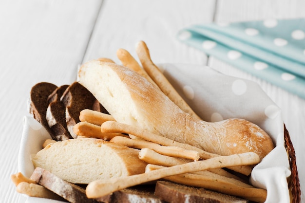 Pão italiano caseiro fresco na cesta com variedade de produtos de padaria de guardanapo azul no espaço livre de fundo branco de madeira