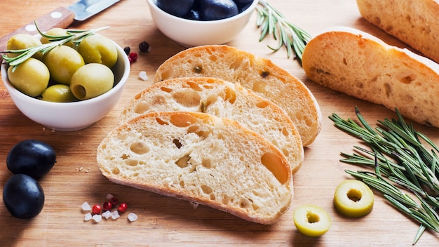 Pão italiano ciabatta com azeitonas e alecrim em uma placa de madeira.