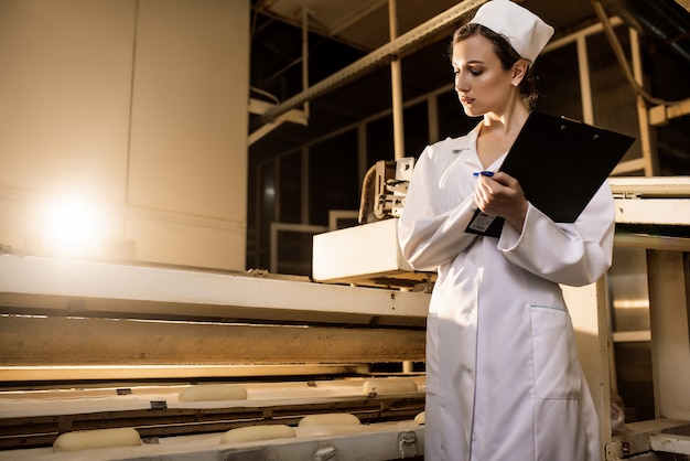 Foto pão. linha de produção de pão. mulher de uniforme. verificação sanitária.