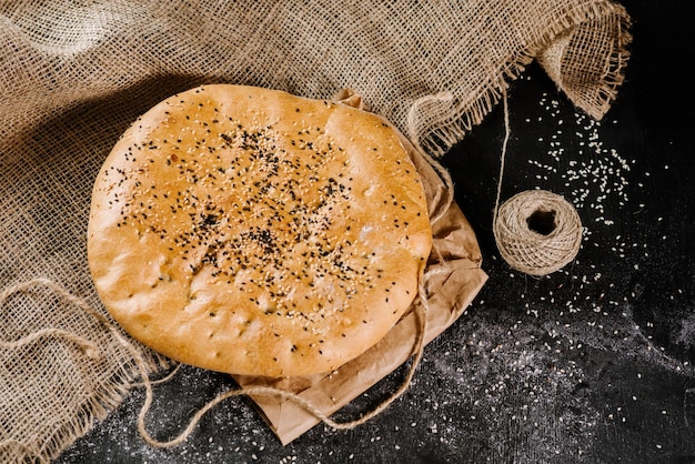 Pão liso arredondado grande fresco na tela no fundo preto de madeira