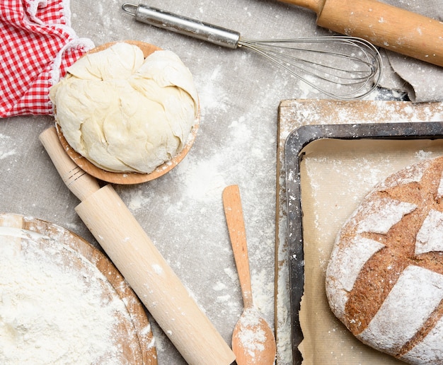 Pão, massa amassada de farinha de trigo branca repousa sobre uma placa de madeira e um rolo de madeira, vista superior